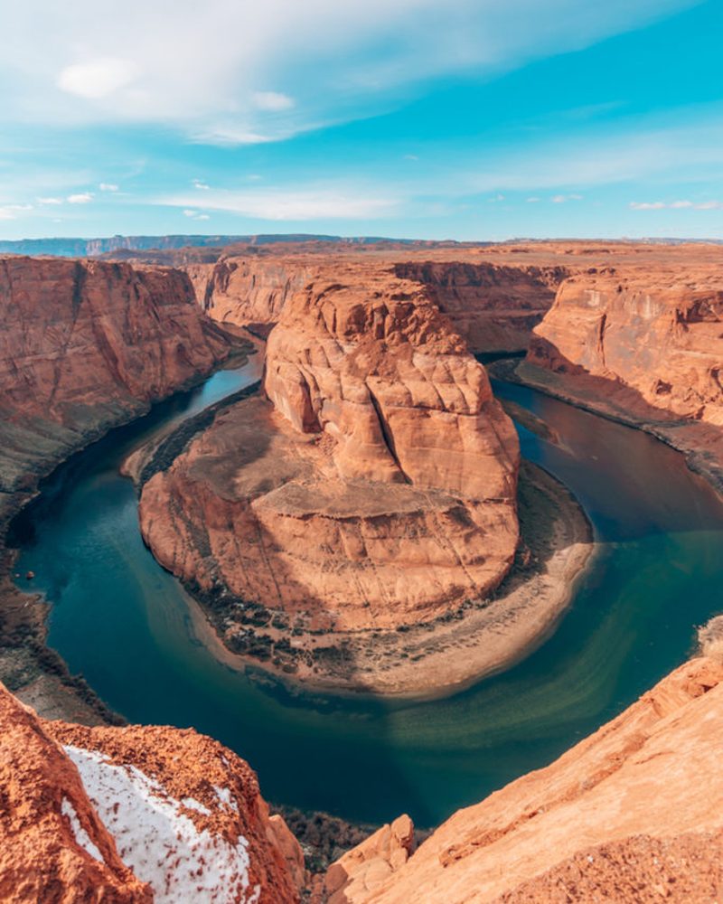 The Colorado River curving around a sandstone butte at Horseshoe Bend under a blue sky